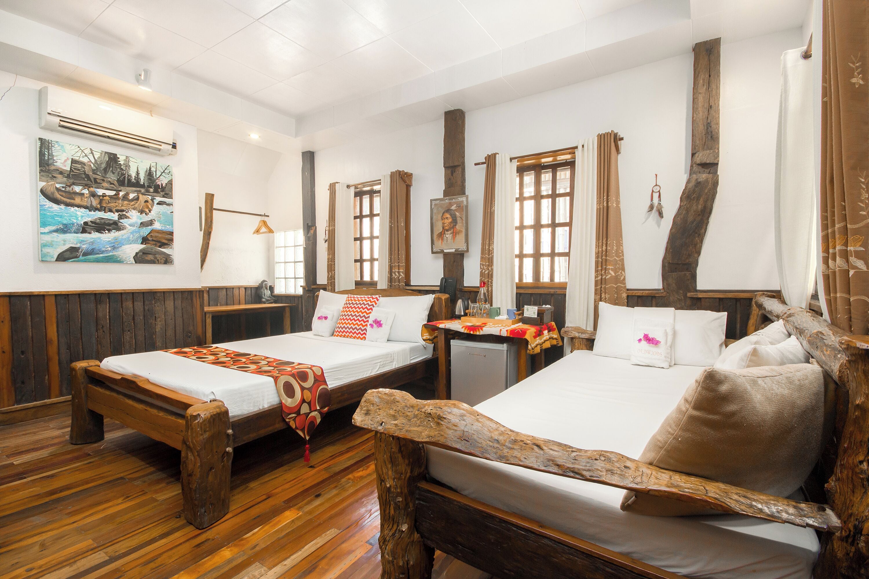 A room with two wooden beds, a small table, and a painting on the wall.