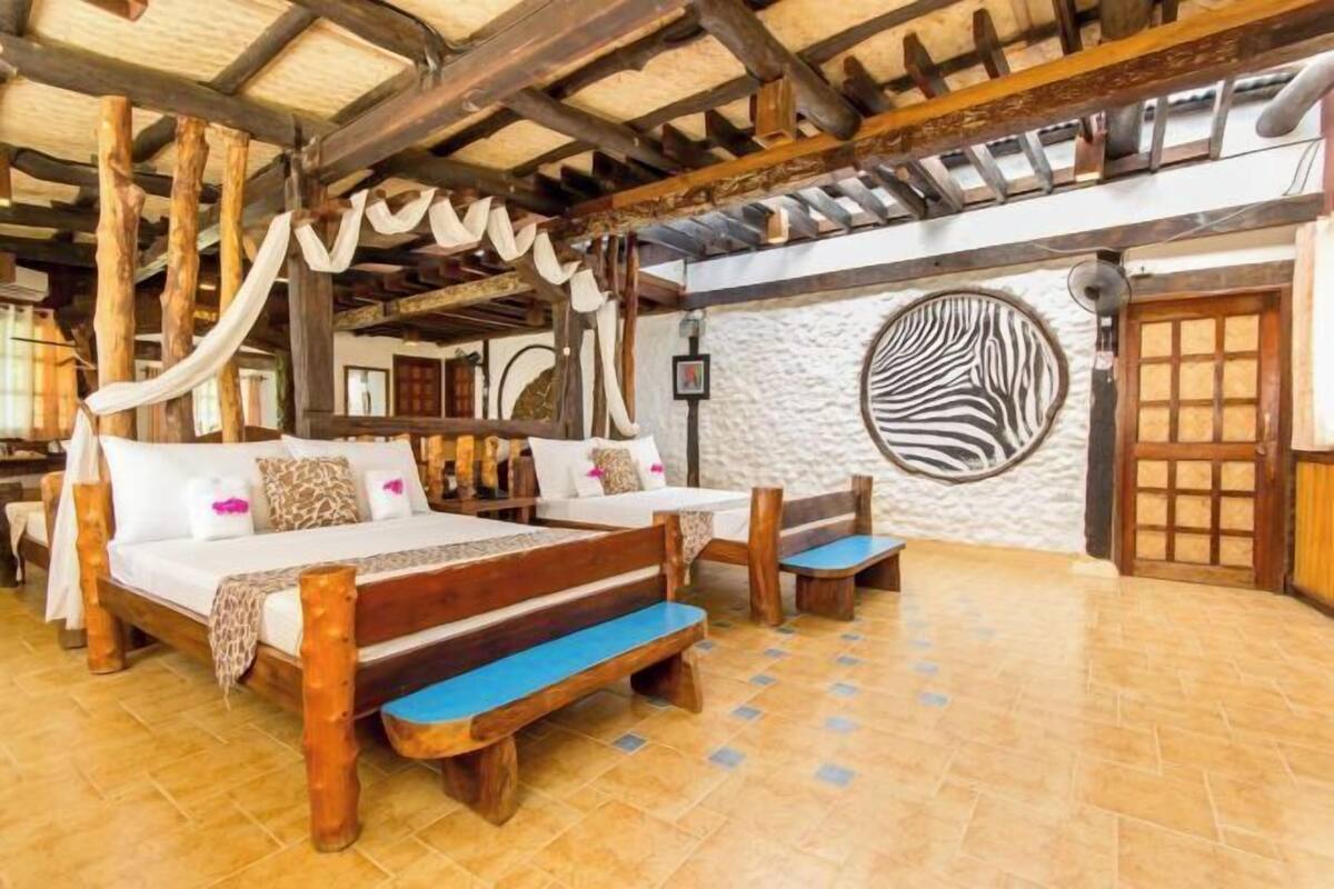 A room with a bed, two benches, a stone wall with a zebra print, and a wooden ceiling.