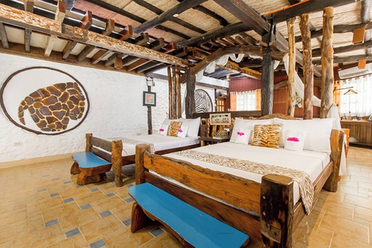 A rustic room with a large bed, two smaller beds, wooden benches, and a unique wall art piece.