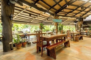 An outdoor dining area with wooden tables and benches, surrounded by potted plants and a thatched roof structure. - Oldwoods by the Sea Nature Resort Bani Pangasinan (Bani)