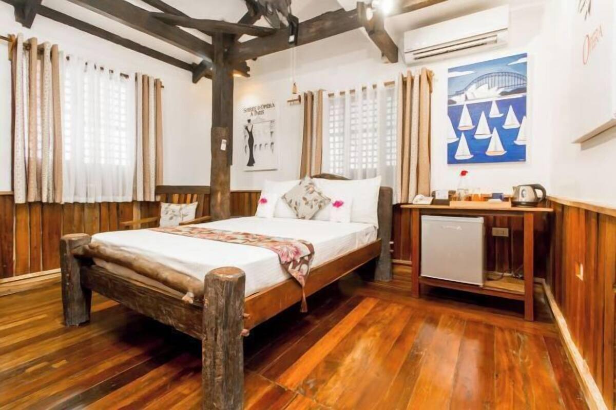 A wooden-framed bed with a white mattress, a small bedside table with a kettle, and a wall-mounted air conditioner.