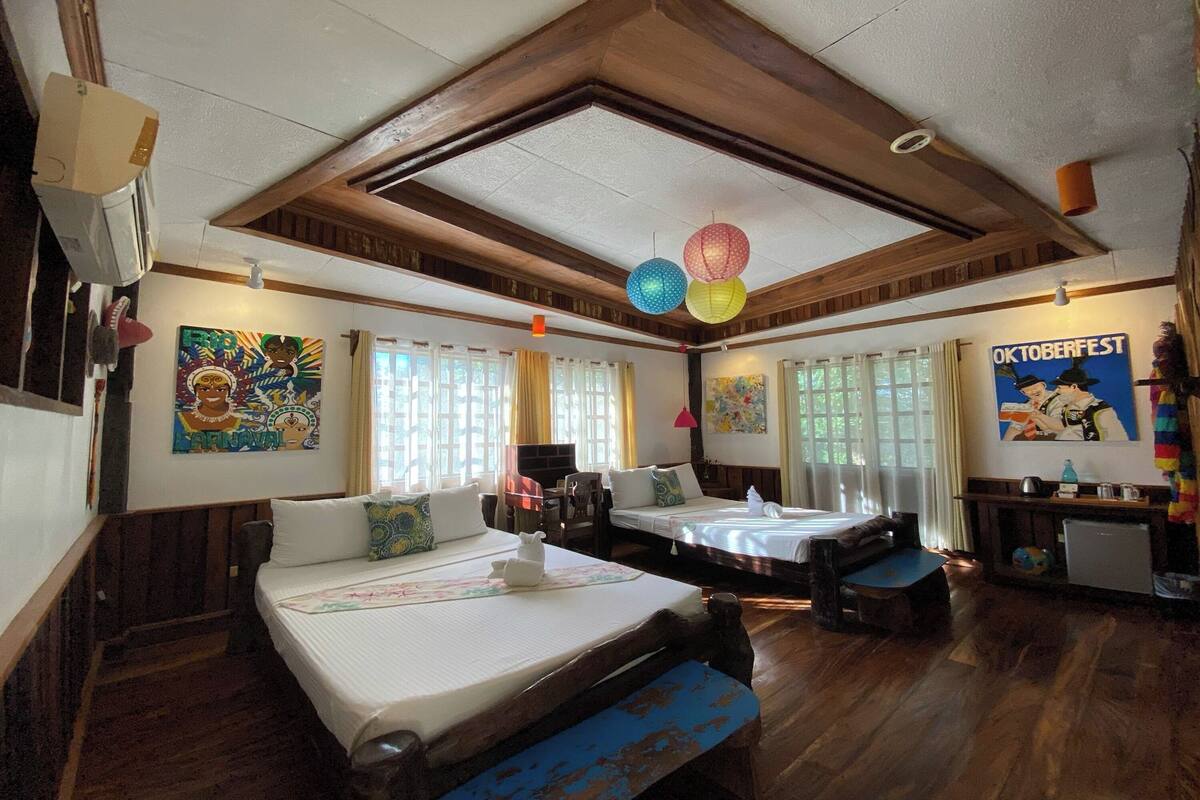 A traditional-style room with wooden floors, two beds with pillows, a small table, and a wall-mounted air conditioner.