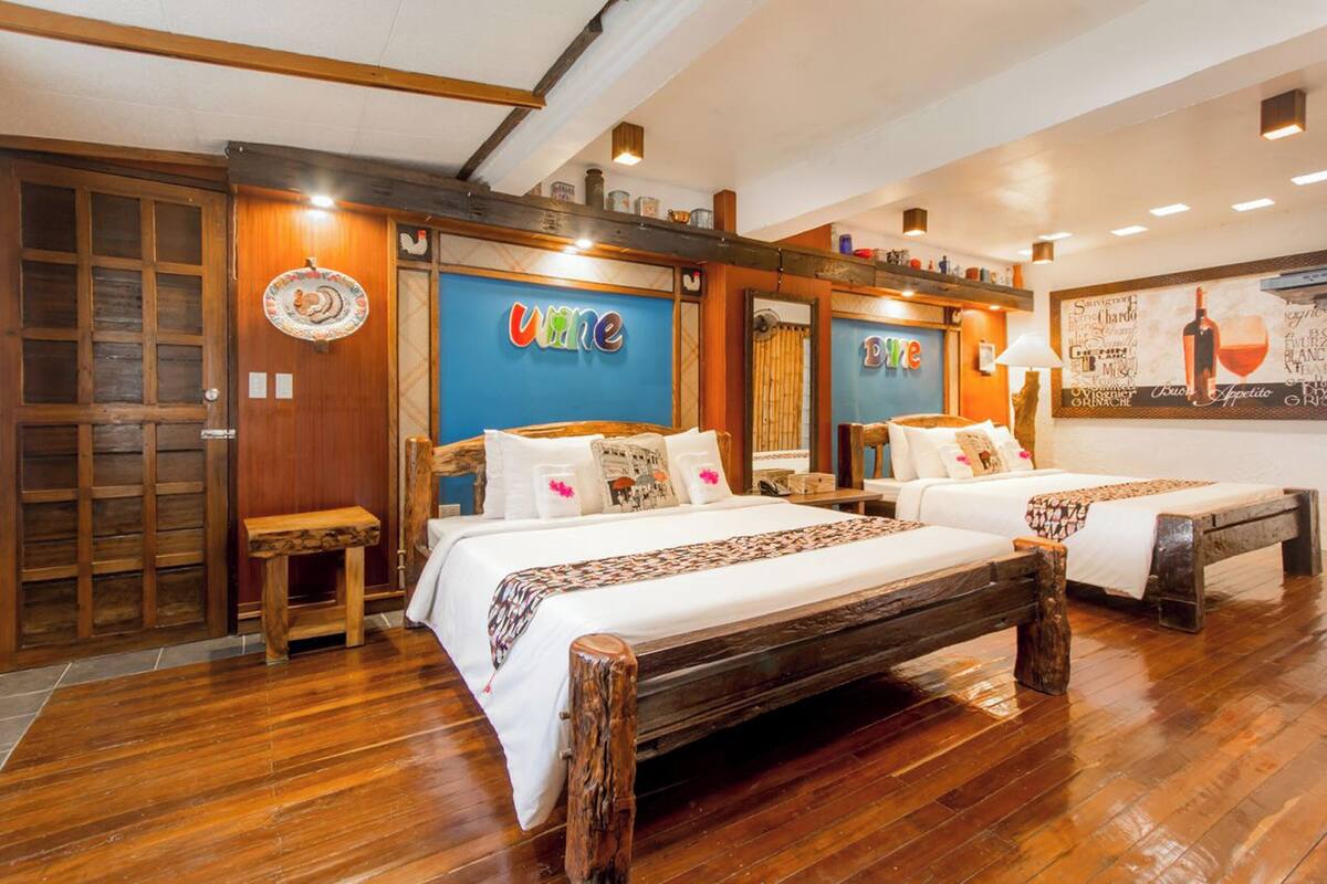 A hotel room with two beds, wooden flooring, and a large mirror.
