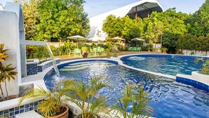 A swimming pool with a waterfall feature, surrounded by potted plants and outdoor seating.