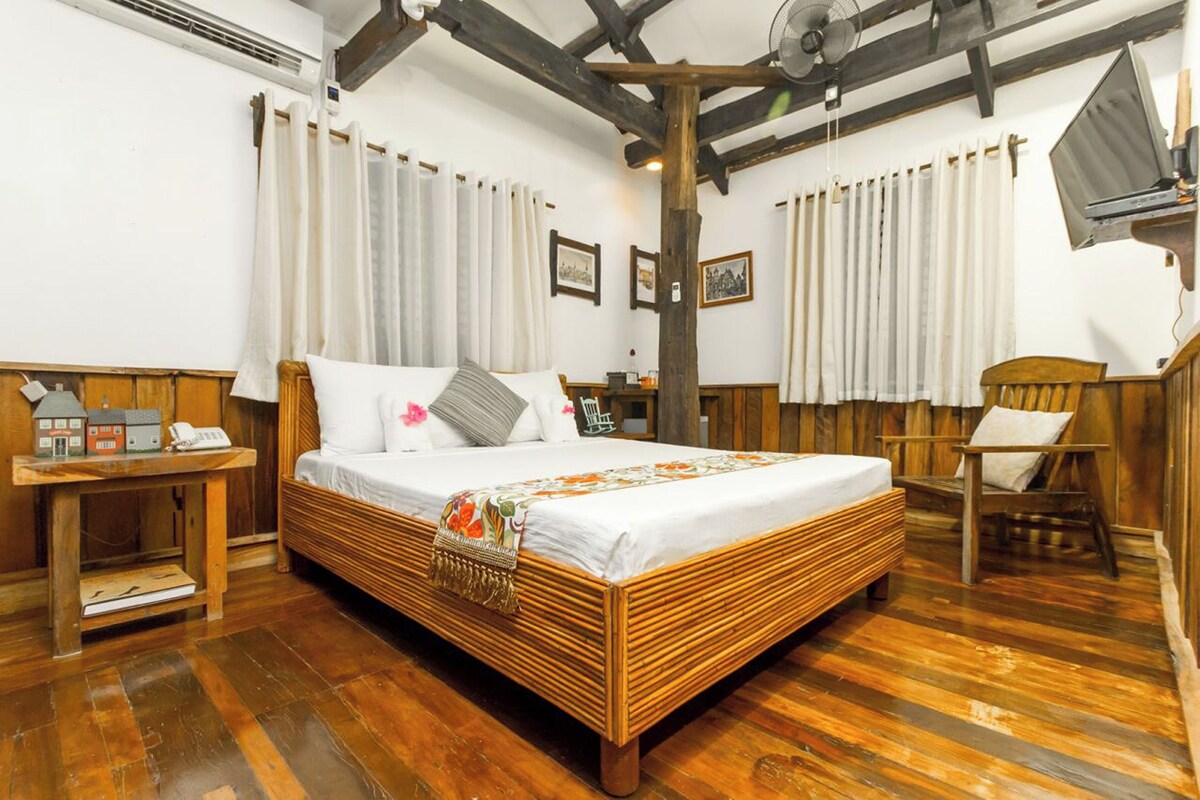 A wooden-framed room with a bed, a small table with a telephone, and a chair.