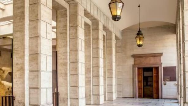 A spacious hallway with stone flooring and columns, leading to a wooden door. - Rome Visits (Rome)