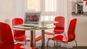 A modern room with a glass table, red chairs, a laptop displaying 'ROME VISITS', and a coffee machine. - Rome Visits (Rome)