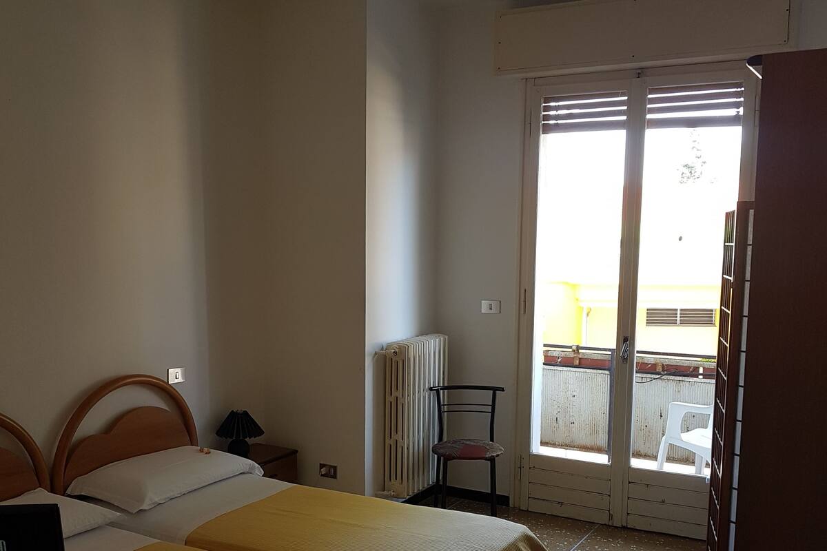 A room with two beds, a desk, a chair, and a radiator.