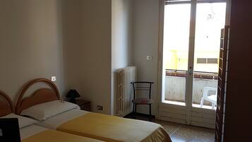 A room with two beds, a desk, a chair, and a radiator.