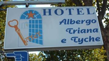 A hotel sign with the name "Albergo Triana e Tyche" and a pointing hand icon.