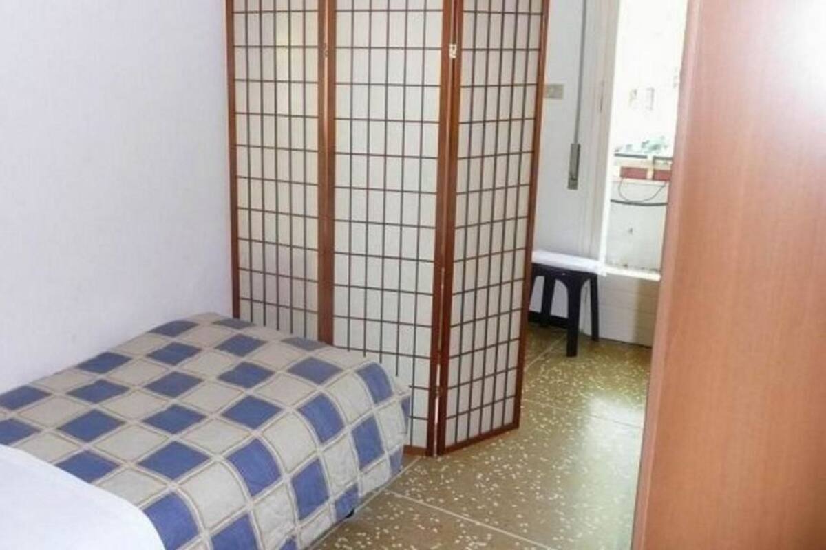 A small, single-bed room with a checkered bedspread, a sliding shoji screen, and a small stool.