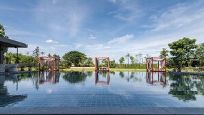 Un área de piscina al aire libre tranquila, con cielo despejado, rodeada de árboles y un césped bien cuidado.