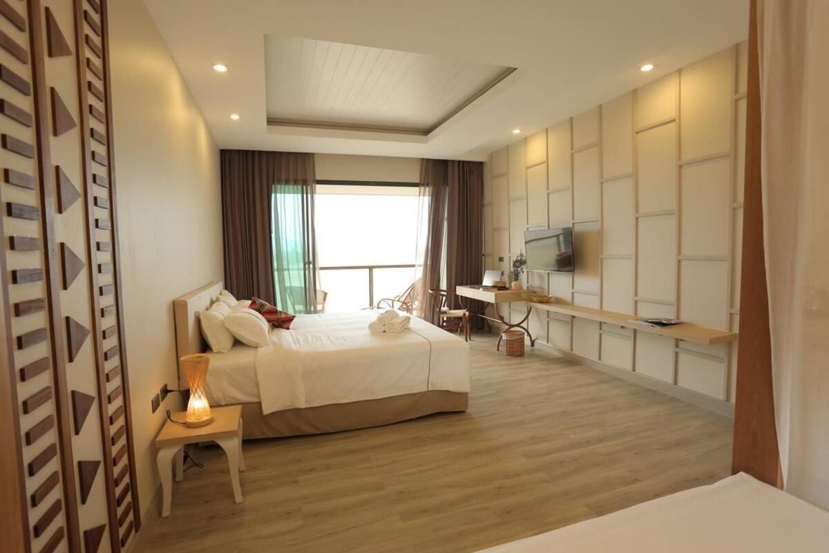 A modern hotel room with a large bed, a desk, a TV, and a view of the outdoors.