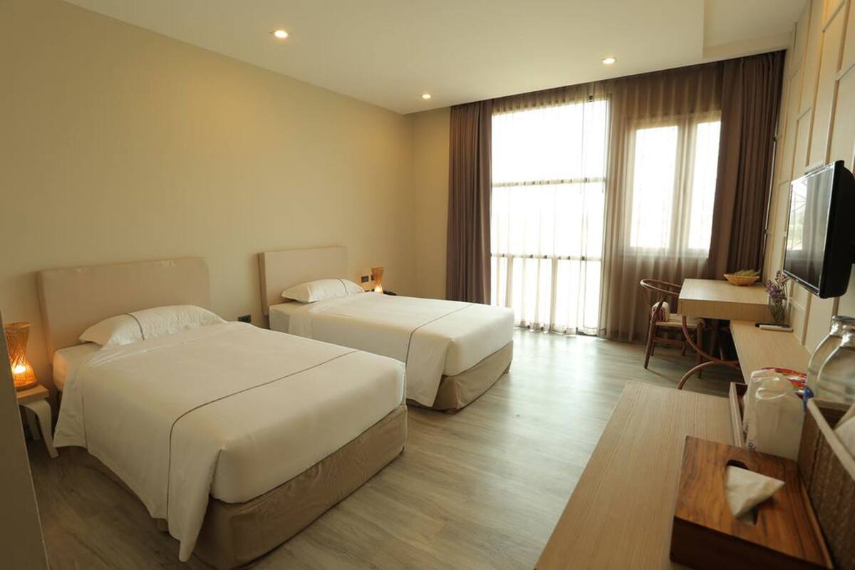A hotel room with two beds, a desk, a television, and a window with curtains.