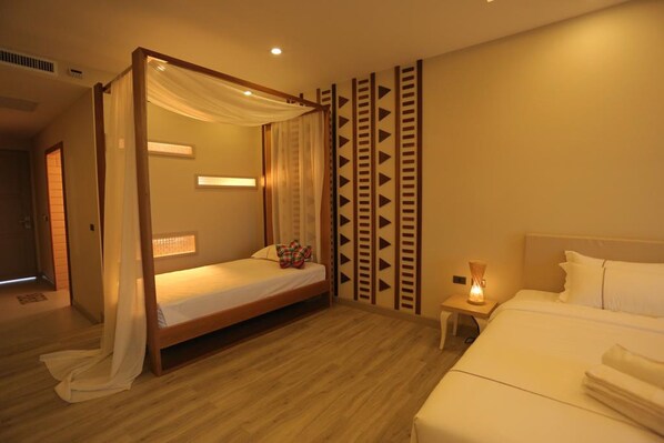 Un dormitorio con cama con dosel, una cama individual más pequeña, una mesita de noche con lámpara y decoración de pared con estampado.