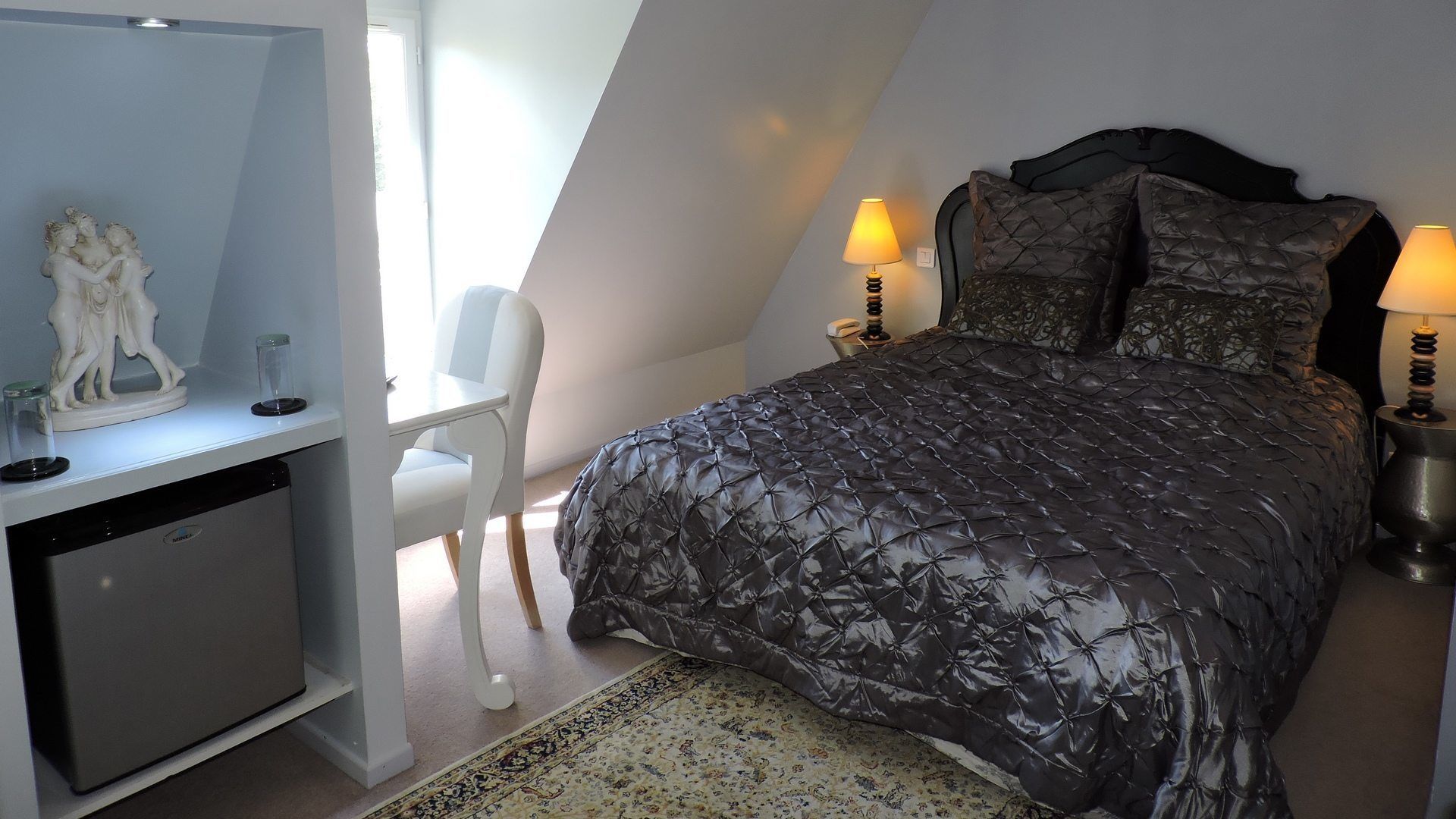 A bedroom with a bed, bedside lamps, a desk, and a chair.