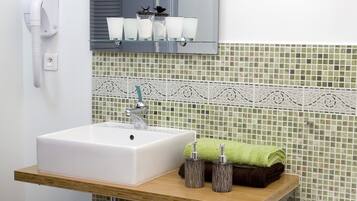 A bathroom with a white sink, a mirror above it, and a green towel on a shelf. There are also two bottles on the shelf.