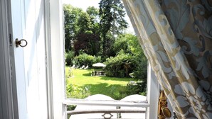 Vista a través de una puerta abierta con cortina estampada, mostrando un jardín exuberante con césped, árboles y una mesa con sillas.