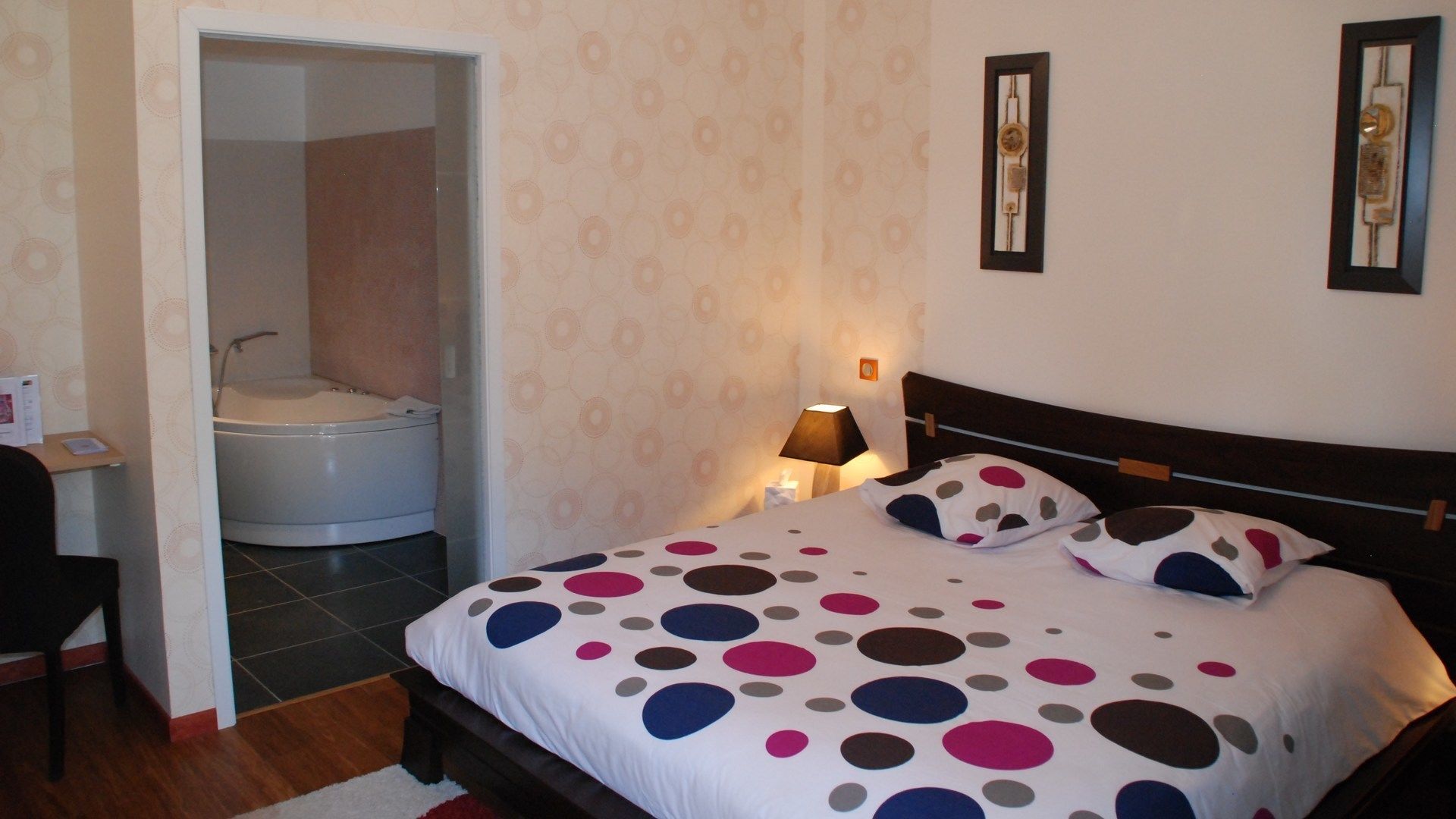 A bedroom with a bed, a bedside lamp, a nightstand, a chair, and a bathroom with a bathtub and toilet.
