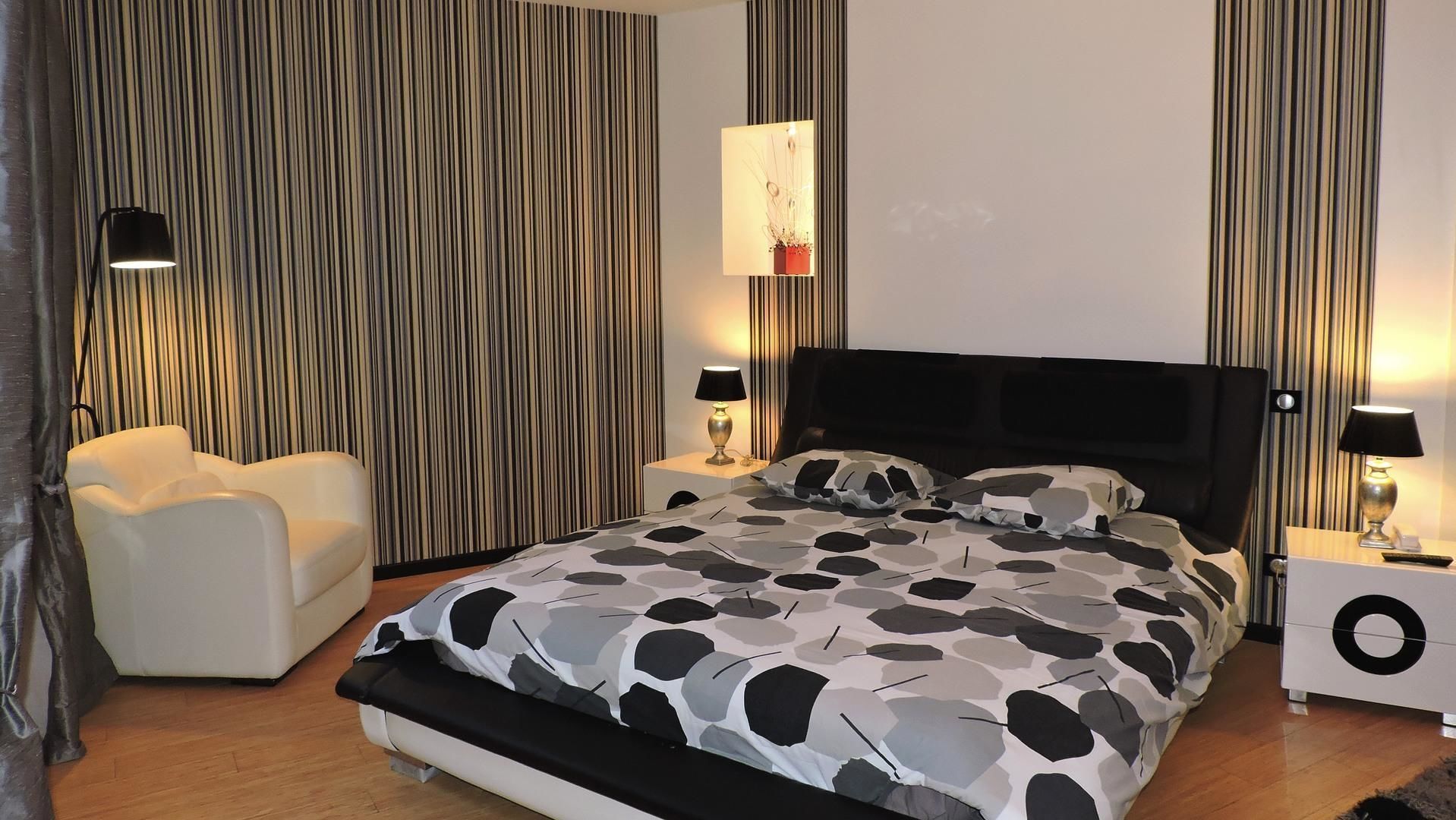 Un dormitorio moderno con una cama grande, dos mesitas de noche, una silla y un telón a rayas.