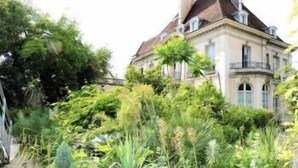 Un edificio grande y histórico con un estilo arquitectónico clásico, rodeado de abundante vegetación.