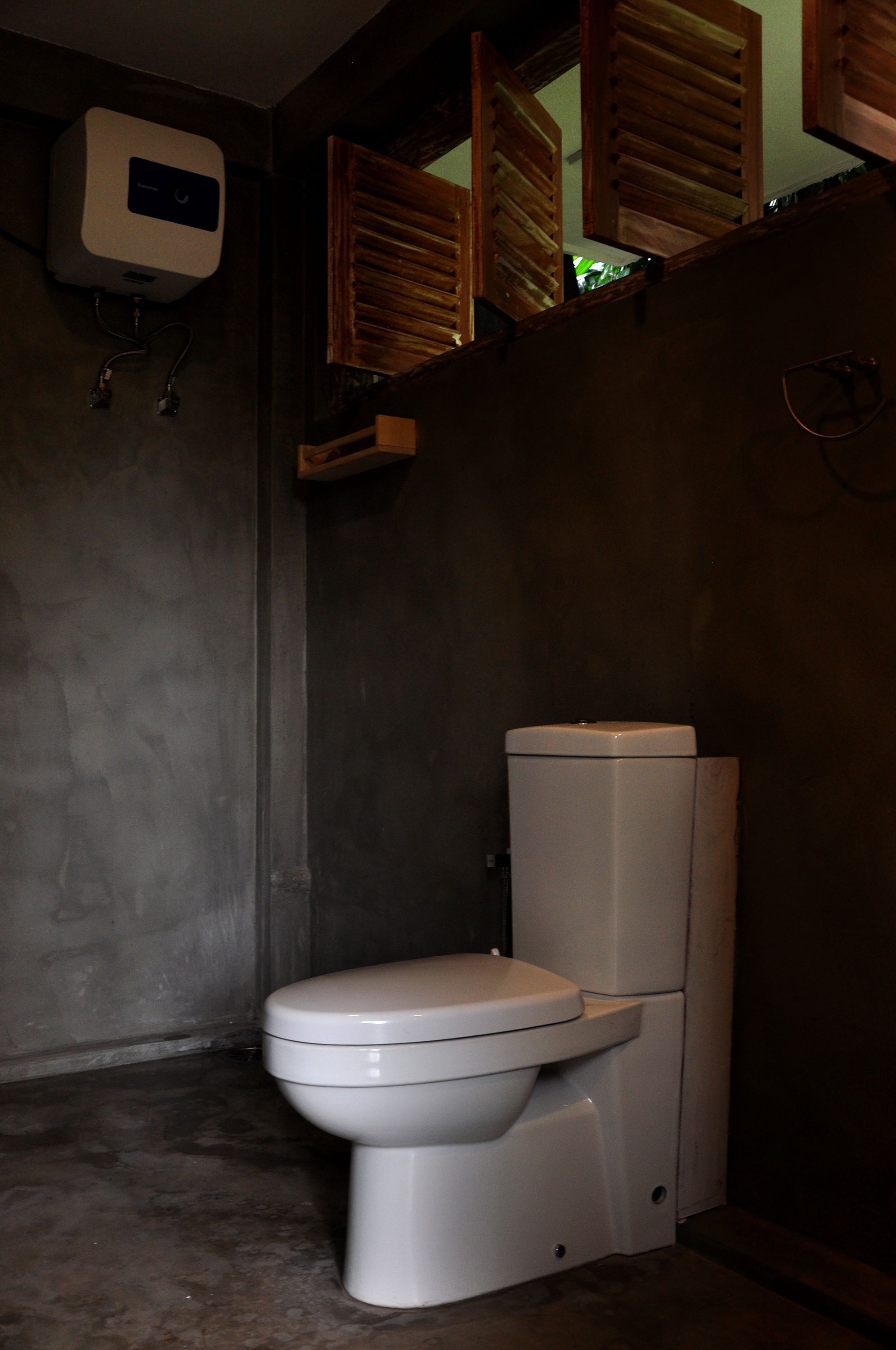 Une petite salle de bain avec des toilettes blanches, un purificateur d’air fixé au mur et des volets en bois à la fenêtre.