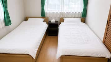 Ein Zweibettzimmer mit zwei Einzelbetten, einem Nachttisch und einem Fenster mit Vorhängen.