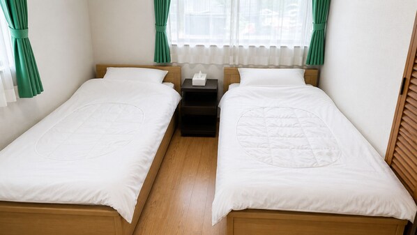 Habitación doble con dos camas individuales, una mesita de noche y ventana con cortinas.