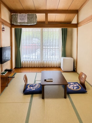 A traditional Japanese room with tatami flooring, a low table, two cushions, a television, and a radiator. - Yamanakako Ryokan RYOZAN (Yamanakako)