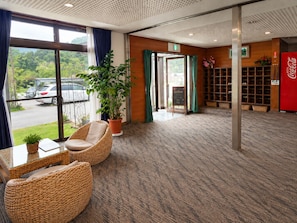 A hotel lobby with wicker furniture, a potted plant, a Coca-Cola refrigerator, and a view of parked cars outside. - Yamanakako Ryokan RYOZAN (Yamanakako)