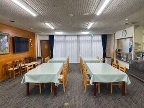 A conference room with two long tables, wooden chairs, a clock, and a kitchen area with a sink and stove. - Yamanakako Ryokan RYOZAN (Yamanakako)