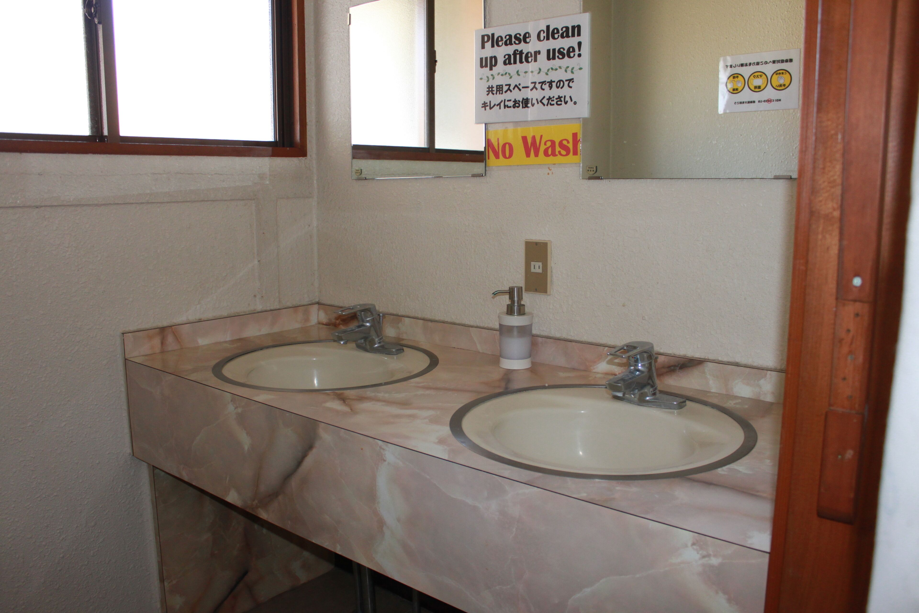 A bathroom with two sinks, a mirror, and a 'Please clean up after use!' sign.