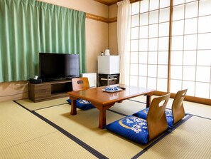 A traditional Japanese room with tatami flooring, a television, a refrigerator, and a table with cushions. - Yamanakako Ryokan RYOZAN (Yamanakako)