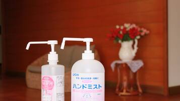 Two bottles of hand sanitizer on a wooden table with a vase of flowers in the background.