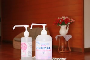 Two bottles of hand sanitizer on a wooden table with a vase of flowers in the background.