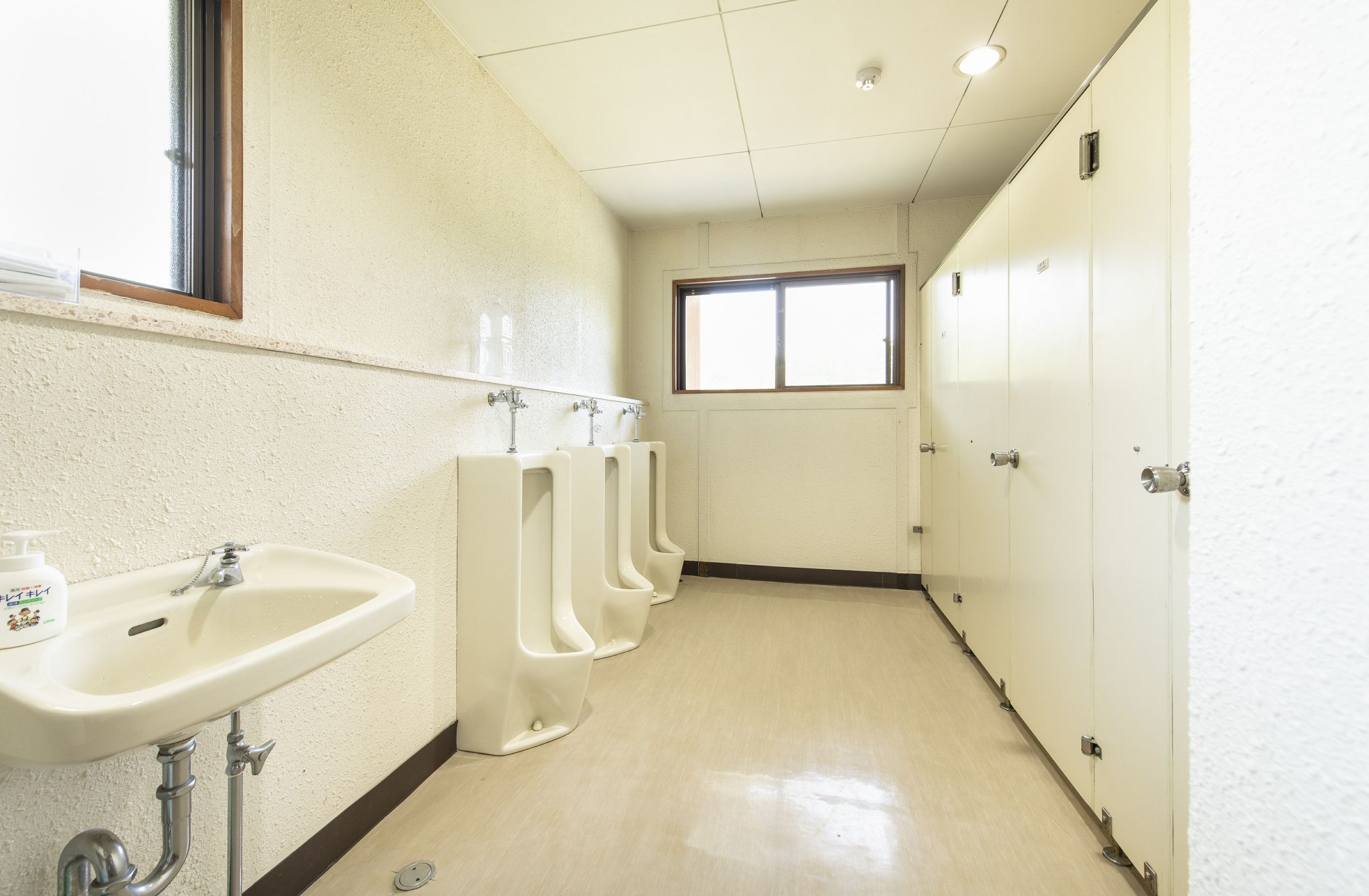 Een toiletruimte met een wastafel, urinoirs en een raam.