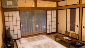 A traditional Japanese-style room with tatami flooring, a futon bed, a television, and a table with a tray of items. - Yamanakako Ryokan RYOZAN (Yamanakako)
