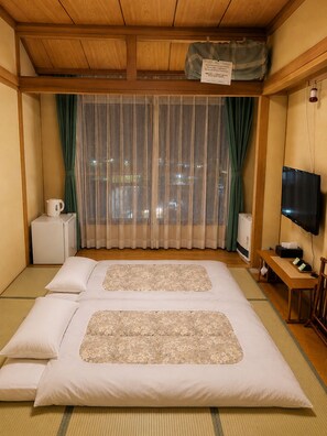 A hotel room with a bed, a television, a small table, and a window with curtains. - Yamanakako Ryokan RYOZAN (Yamanakako)
