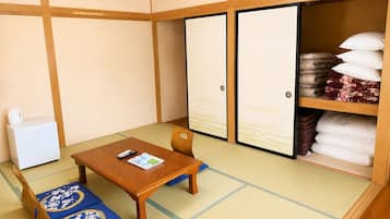 Um quarto japonês tradicional com tatames, uma mesa de madeira baixa, uma cadeira, um guarda-roupa e uma estante com roupa de cama.