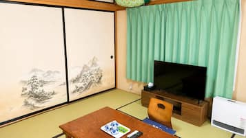 A traditional Japanese room with tatami flooring, a television, a wooden table with a remote control, and a green curtain.