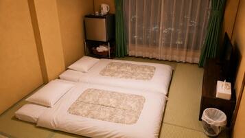 Hotelkamer met twee bedden, een kleine tafel met waterkoker, een prullenbak en uitzicht op de stad 's nachts.