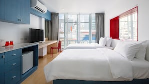 A hotel room with a bed, a desk with a TV, a mini-fridge, and a view of the city. - 128 Room And Massage (Bangkok)