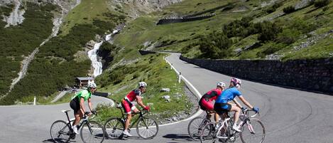 A group of cyclists on a winding mountain road with a waterfall in the background.