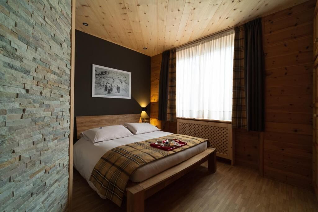 A wooden-paneled room with a bed, a wall-mounted picture, and a window with curtains.