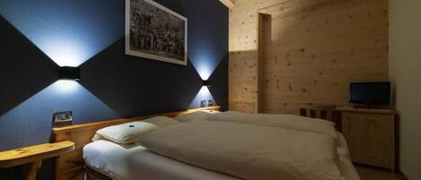 A bedroom with a bed, bedside tables, a wall-mounted picture, and a television.