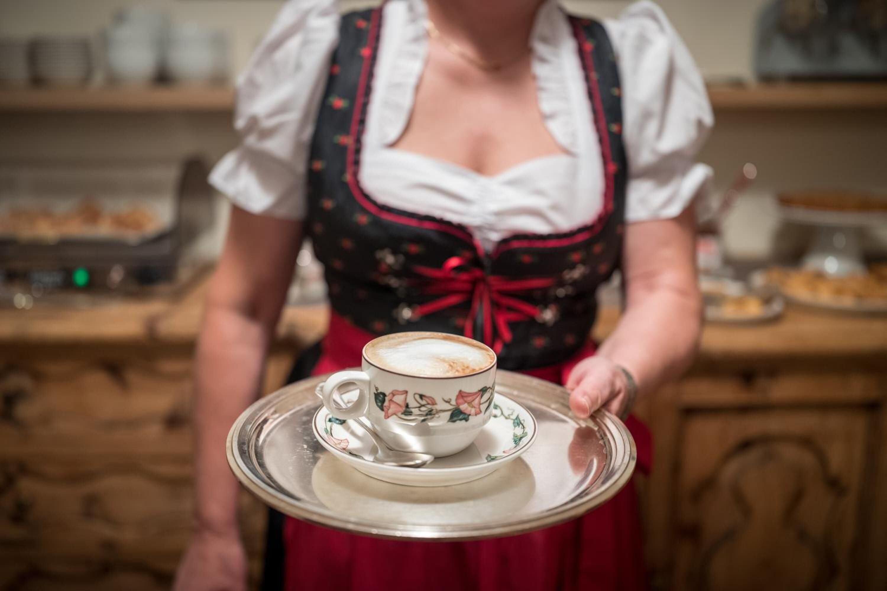 Une personne vêtue d’un costume traditionnel tenant un plateau sur lequel se trouve une tasse de café.