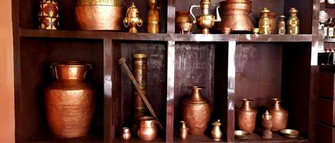 A wooden shelf with various copper and metal kitchenware, including pots, pans, and utensils.