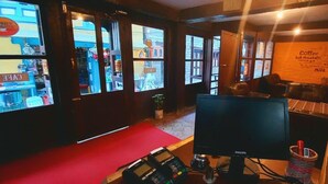 Un café chaleureux avec un tapis rouge, un grand écran et un tableau affichant les différentes sortes de café et les options de lait disponibles.