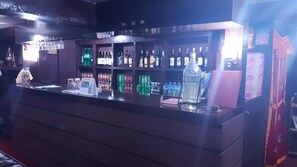 Un espace bar avec des étagères remplies de différentes bouteilles et canettes, une caisse enregistreuse et un grand distributeur d’eau.