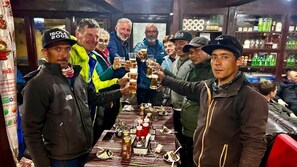 Un grupo de personas brindando con vasos de cerveza en una mesa con varias botellas y copas.
